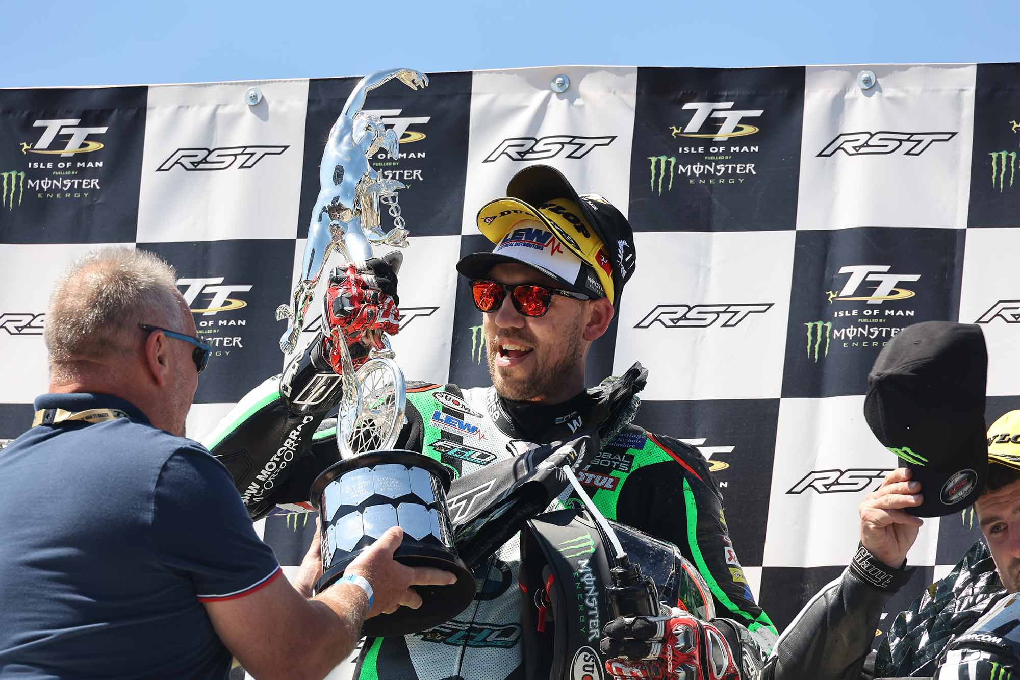 Peter Hickman hoisting one of four trophies (and three sponsor hats) he earned at IoM TT.