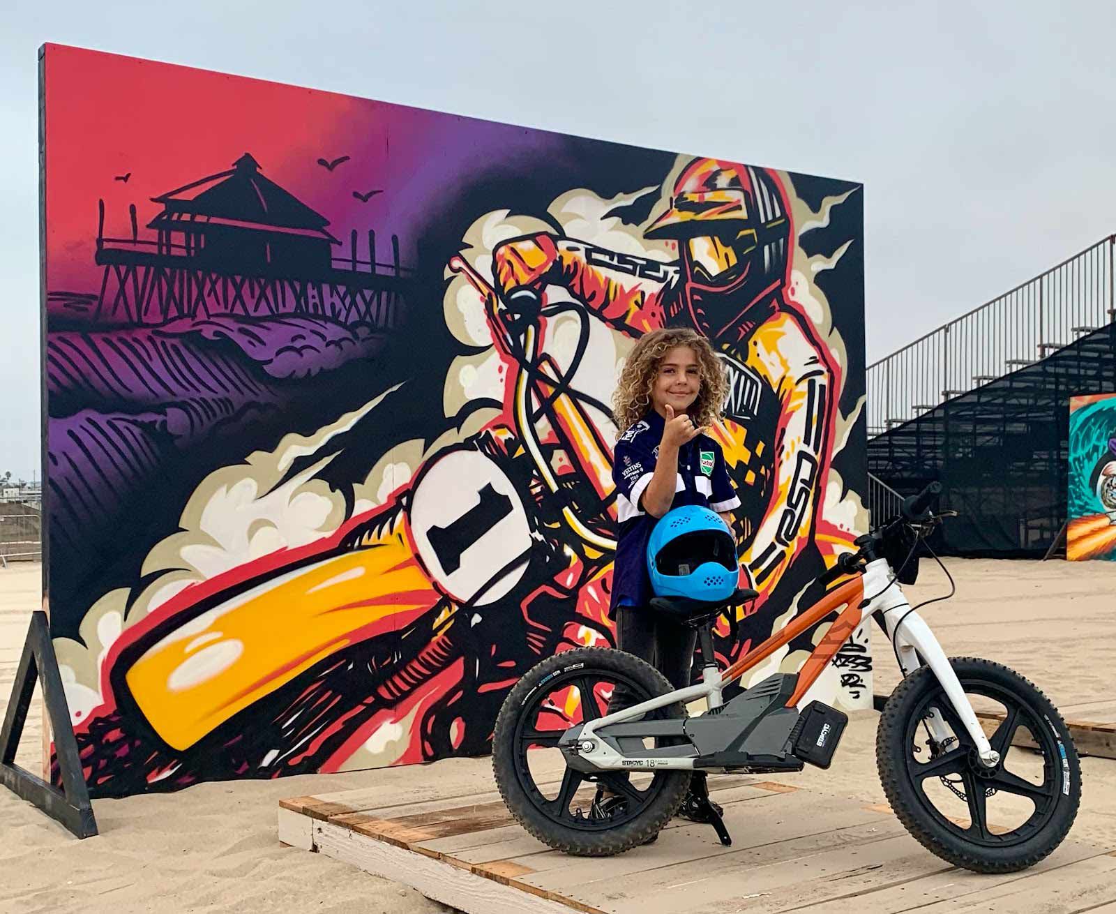 Stacyc champion racer posing in front of Josh Pena’s incredible “Moto Flow” artwork during event setup.